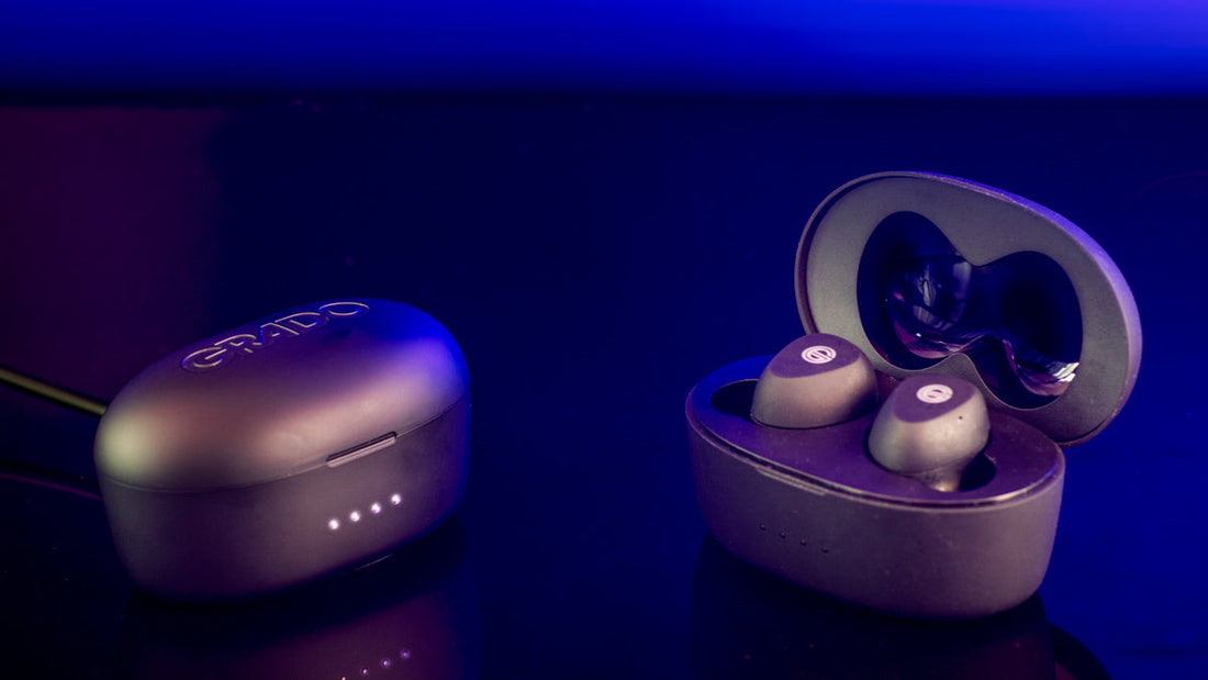 Photo of two sets of the GT220 wireless earbuds in their cases sitting on a table. One pair is open so you can see the earbuds with the white - G - logo on top. There is a blue background on the image. 