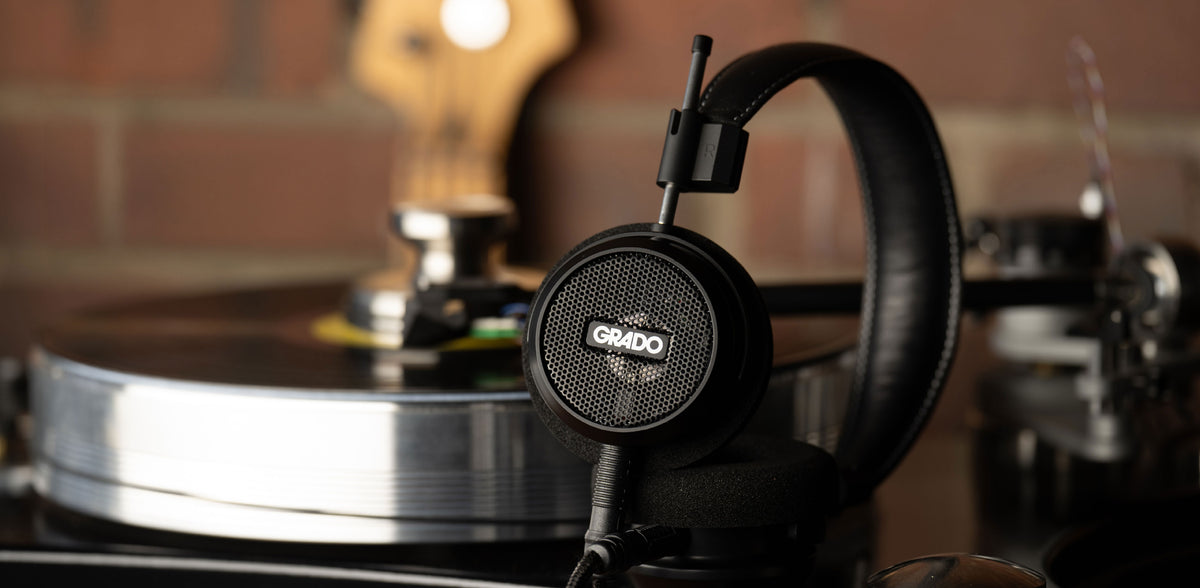 Photo of the S150 Headphones resting next to a turntable in front of a red brick wall.